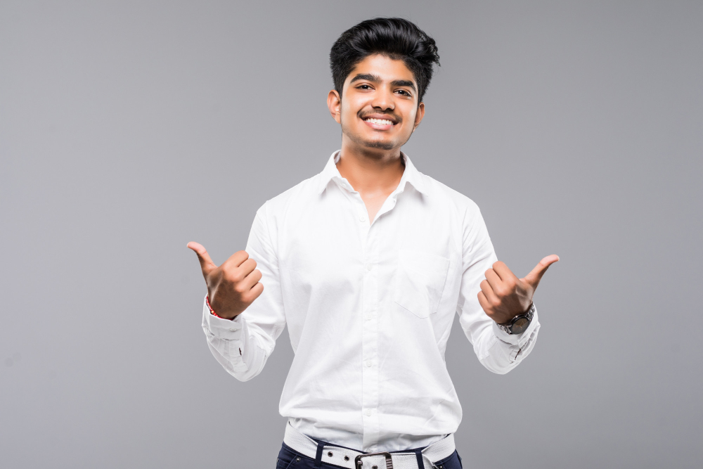 young indian man standing isolated grey wall approving doing positive gesture with hand thumbs up smiling happy success